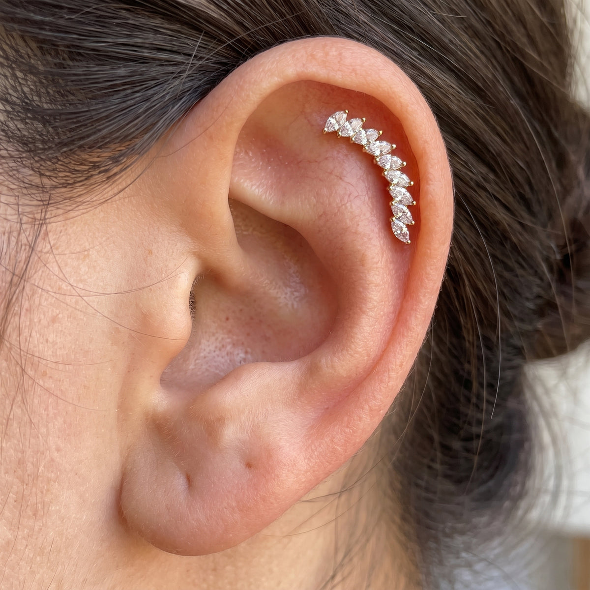 Close-up of Arcturus gold marquise earring worn along the upper ear, following the curve of the helix