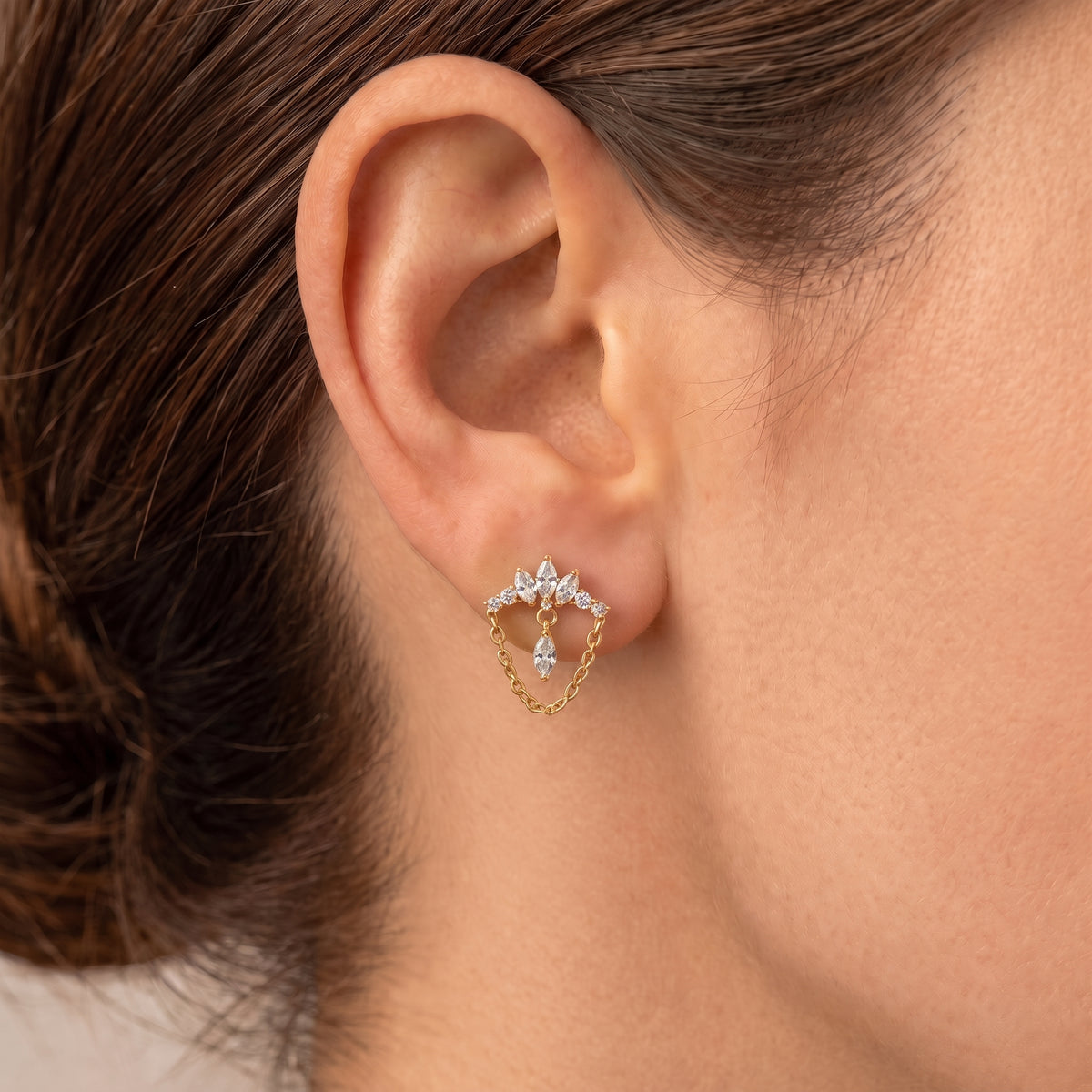 Close-up of Diadem gold flat-back earring on an earlobe, chain curving below the crown
