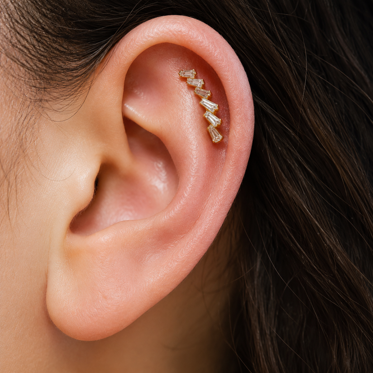 Close-up of Glacia gold baguette earring worn along the upper ear, following the curve of the helix