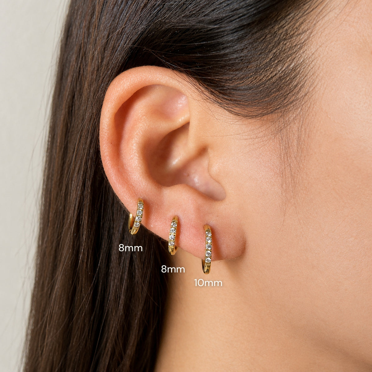 Three Halo gold huggie hoops stacked on one ear — two Halo 8mm on the upper holes and one Halo 10mm on the lower lobe, labeled by size